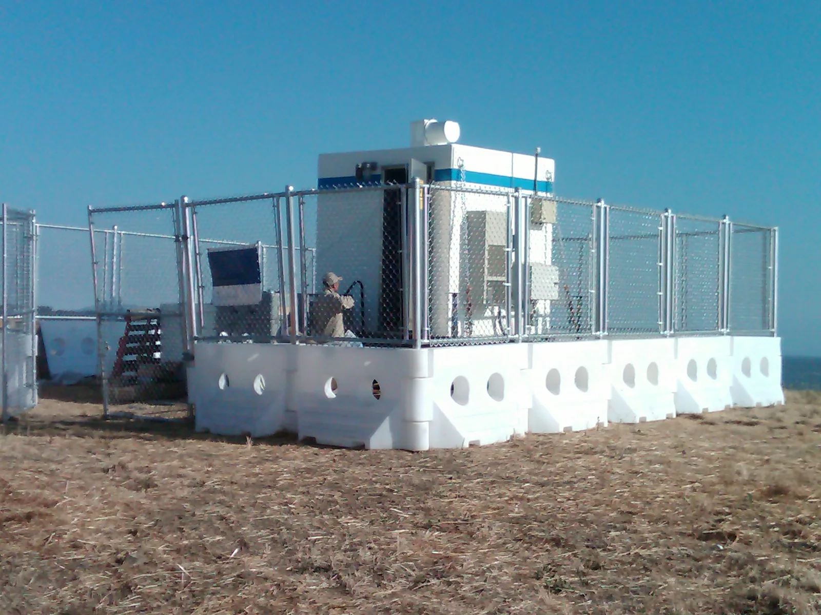 White WATERCADE barriers with chain-link fence panels around equipment at a work site