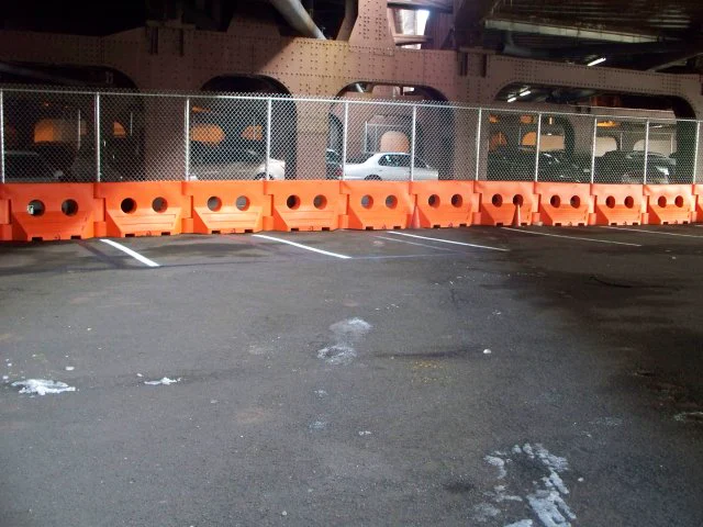 Orange WATERCADE barriers with chain-link fence panels under a highway overpass