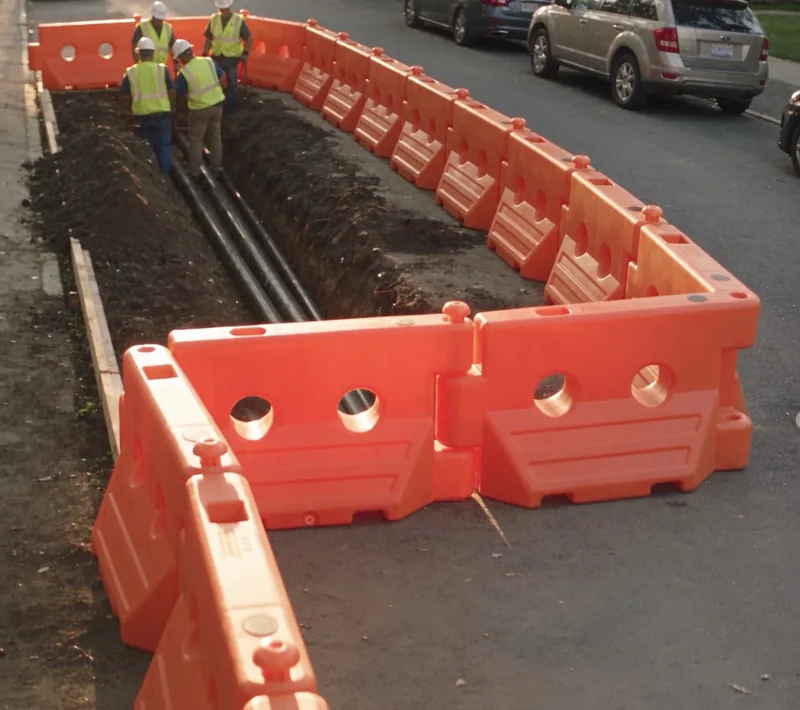 Orange WATERCADE barriers linked with swivel pins around a street trench, turning 90° at the corners